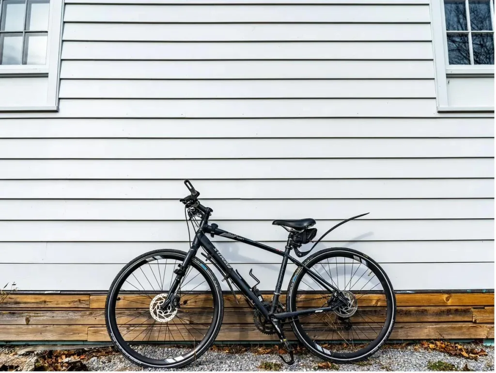 Vélo hybride noir appuyé contre un mur de clin blanc