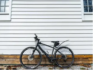 Vélo hybride noir appuyé contre un mur de clin blanc